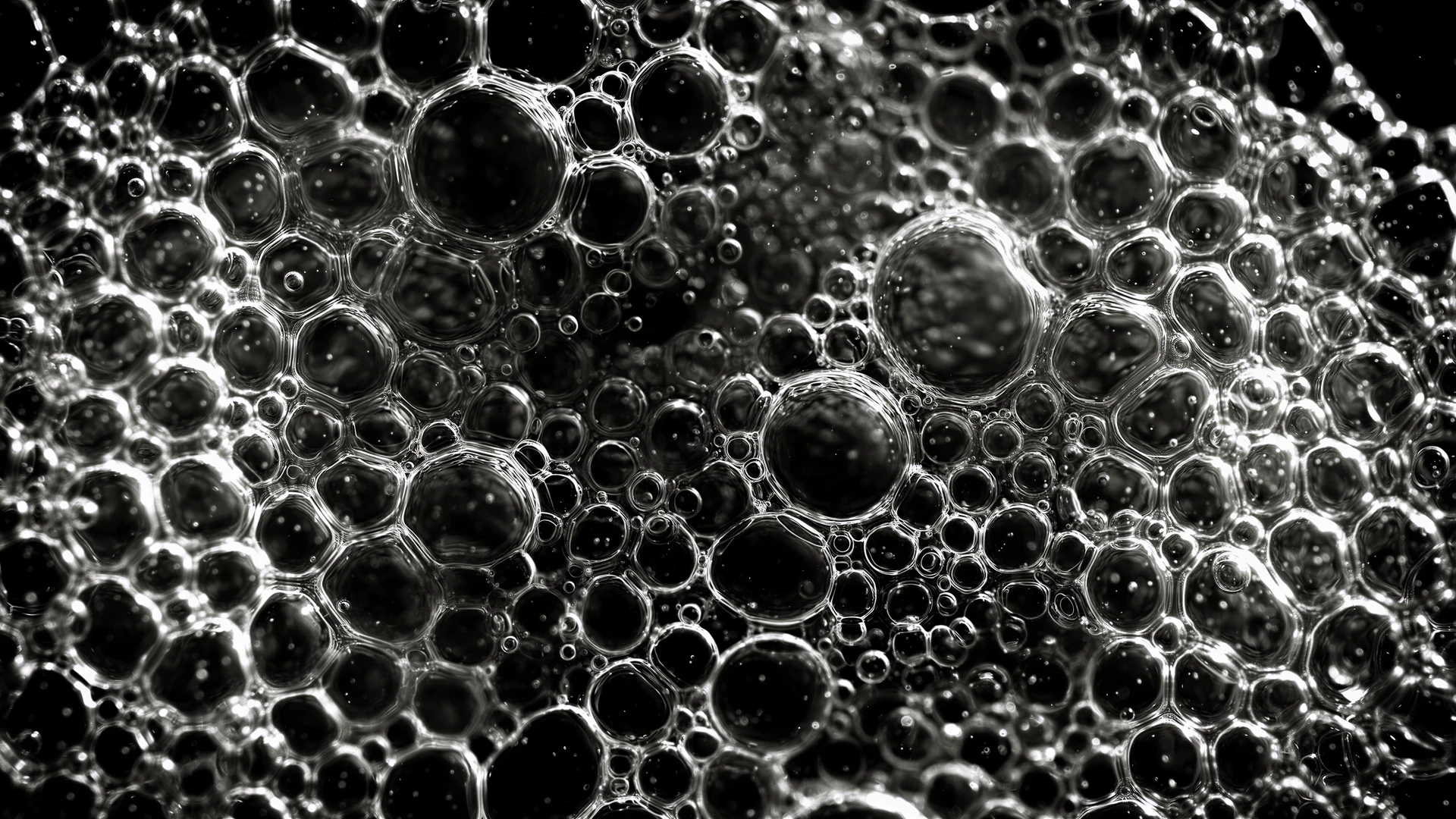 A mesmerizing monochrome field of liquid bubbles glows against deep black. Atomic textures and fluid spheres create a bold, otherworldly abstract wallpaper.