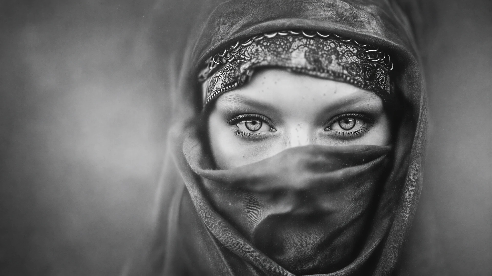 A striking black-and-white portrait of a veiled warrior woman, framed by intense eyes, textured fabric, and moody cinematic light. Film grain adds timeless d…