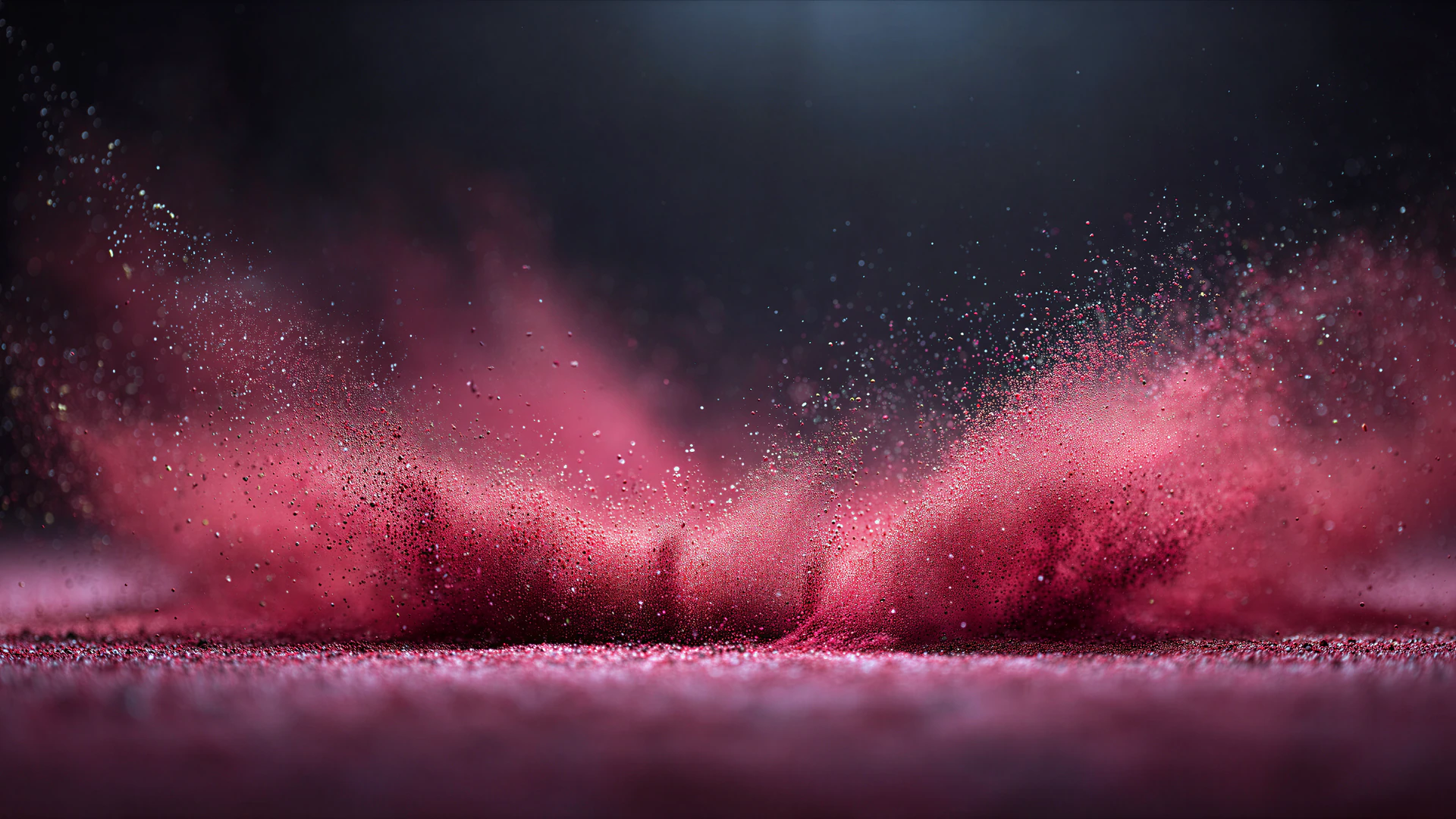 A dramatic macro burst of pink and red powder rises in an elegant arc, glowing against dark clouds and a reflective surface.